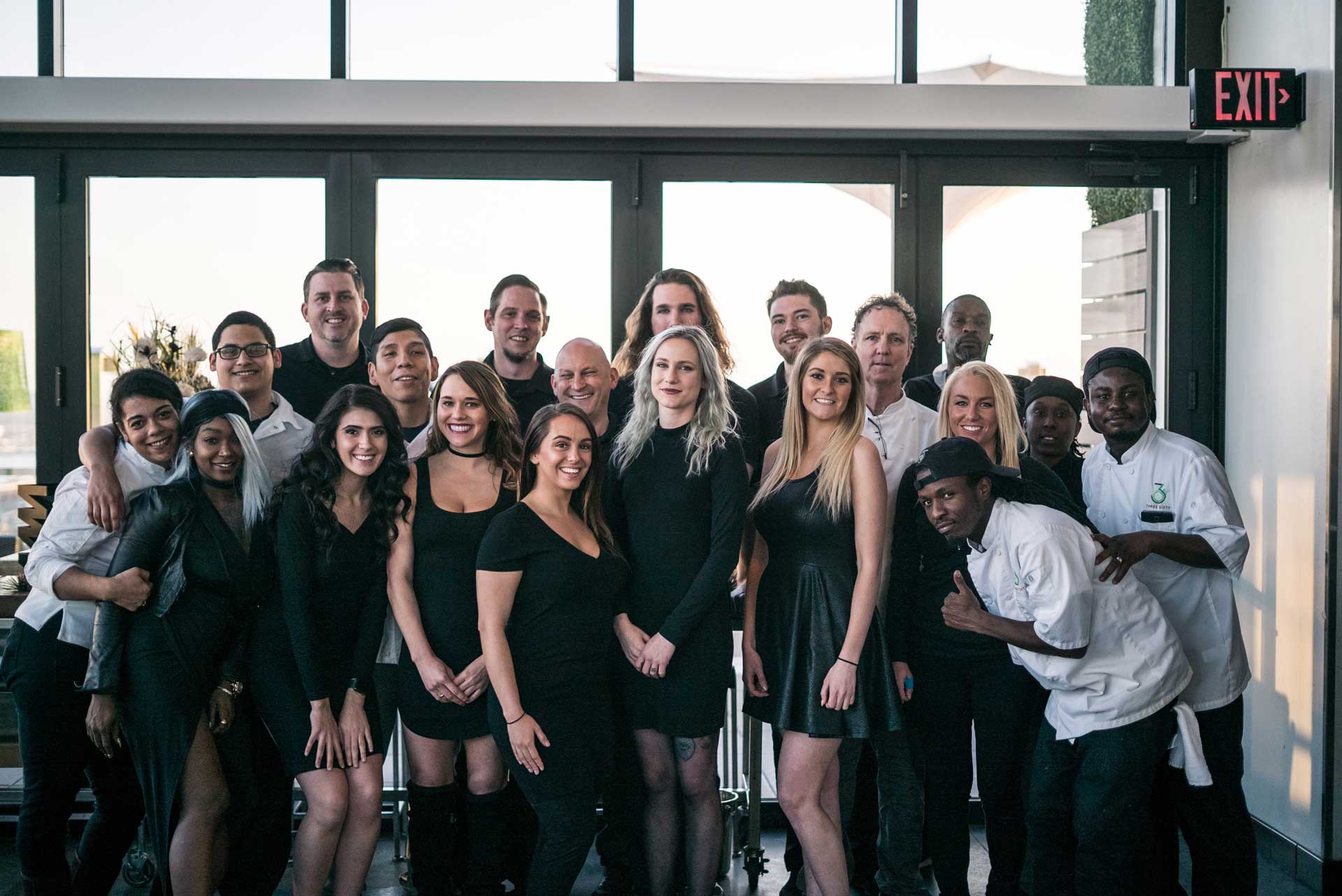 A group of people smiling and posing for a photo in front of large windows, showcasing a bright and cheerful atmosphere